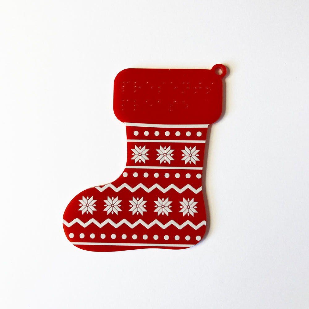 Red and white Christmas stocking with snowflake pattern on a white background with braille text.