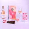 Wine bottle, chocolate bar, wine glass, and other items on a white surface with a pink and white background.