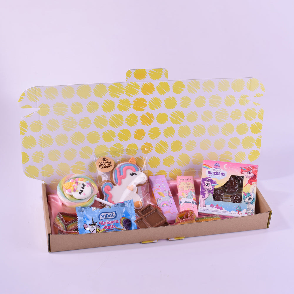Carton box with colorful snacks and a unicorn toy on a light purple background