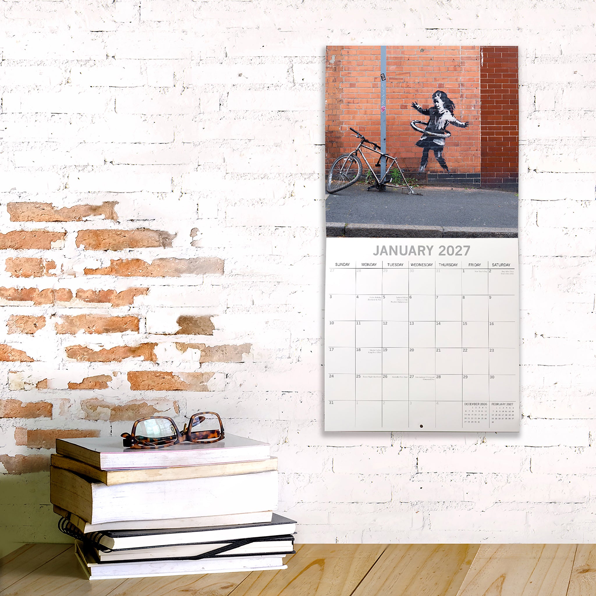 Calendar on a brick wall with books and sunglasses below