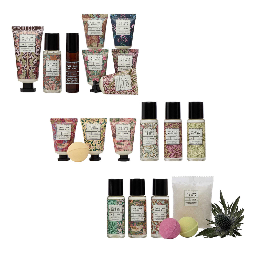 A collection of Bath & Body Works 'Wildflower' scented products arranged on a white background, including patterned hand cream tubes, roll-on bottles, bath bombs, and a bath towel, with small decorative fruit and thistle props.