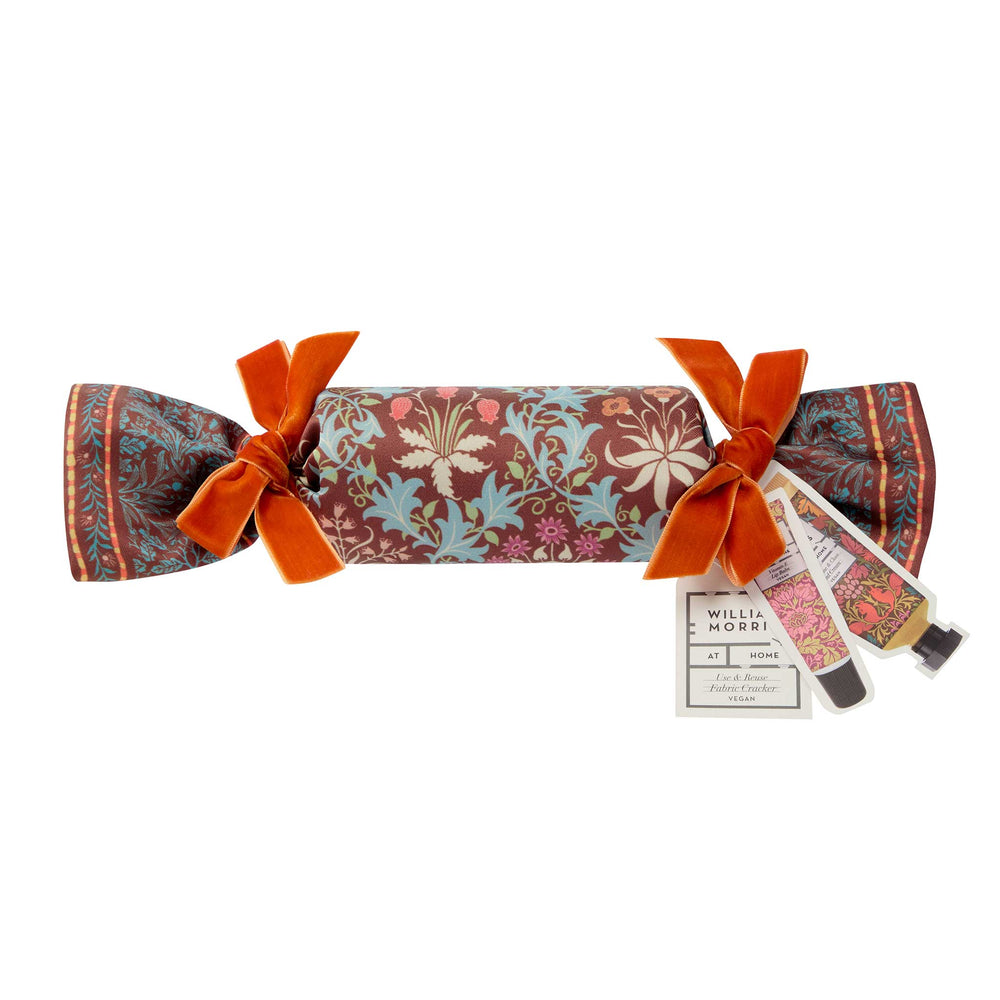 A Willam & Morri Christmas Cracker gift box featuring a floral pattern in rust, light blue, and pink, tied with two orange velvet ribbons and accompanied by a small gift bag and tag on a white background.