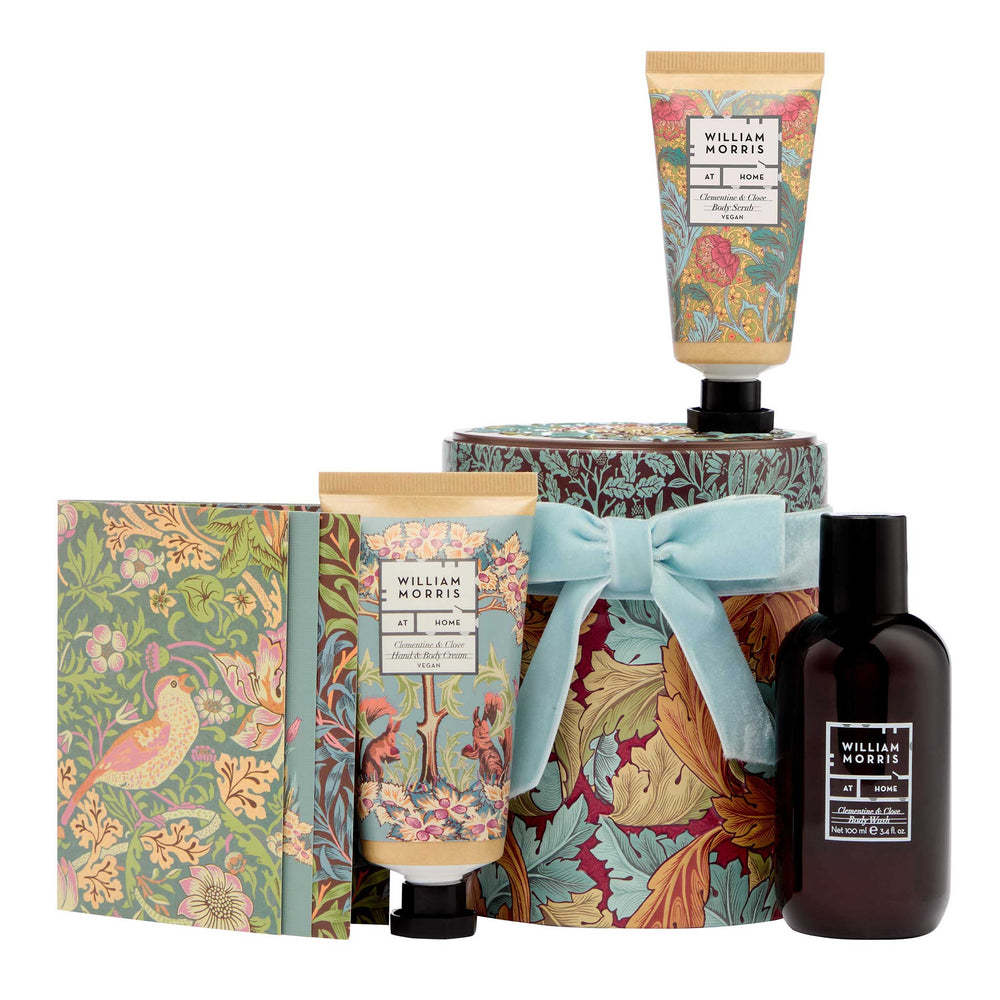 William Morris gift set featuring a bird-patterned box, a floral-patterned hand cream tube, a floral-patterned lotion tube with a light blue ribbon, and a dark amber body wash bottle, all on a white background.