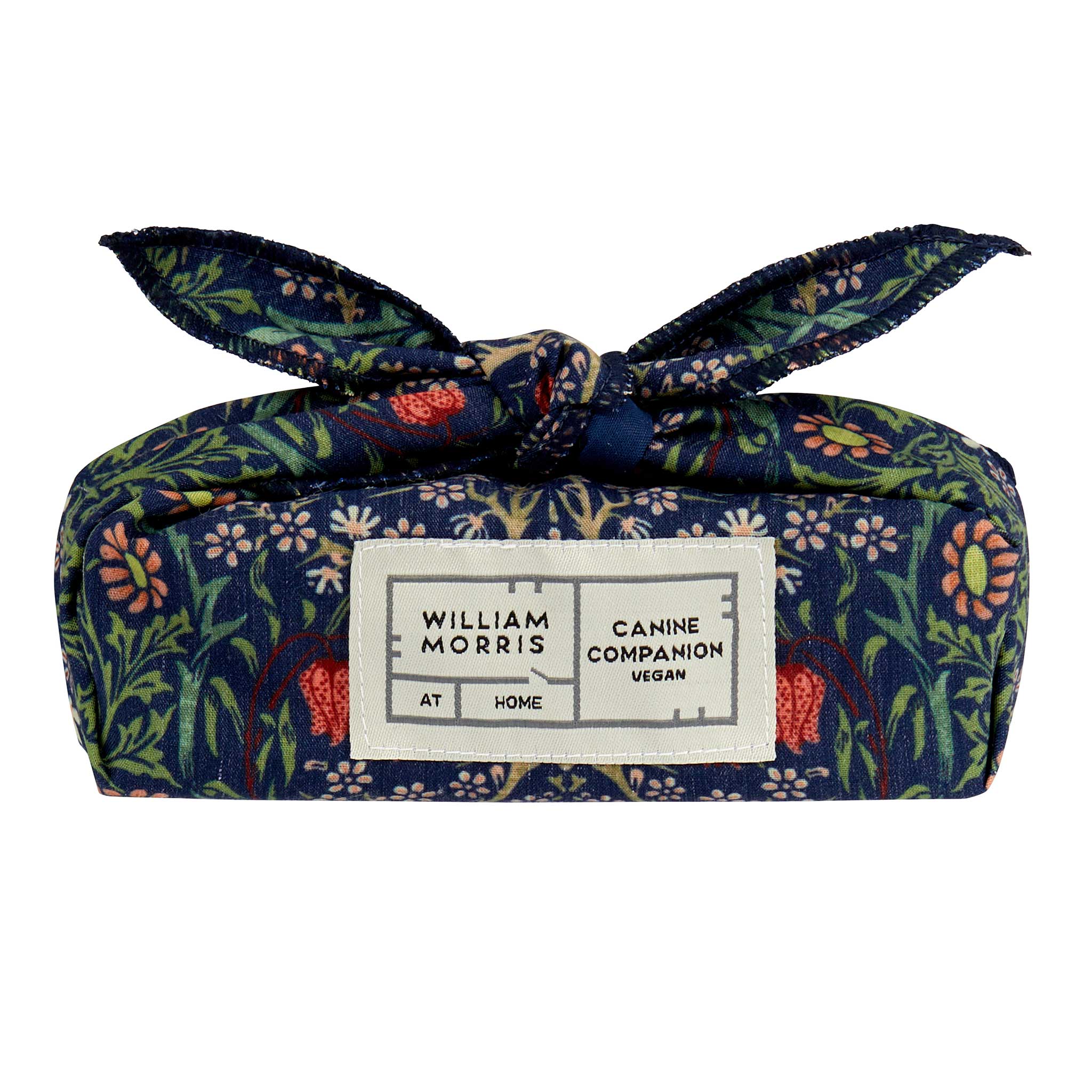 A William Morris Canine Companion vegan wrap gift bag tied in a bow, featuring a navy blue floral pattern with pink, green, and orange accents, and a white brand label on the front.