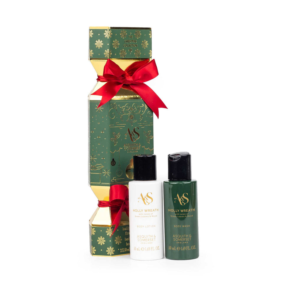 A Christmas-themed gift set from AS Holly wreath, featuring a green and gold box tied with a red ribbon, a small white bottle, and a dark green bottle on a white background.