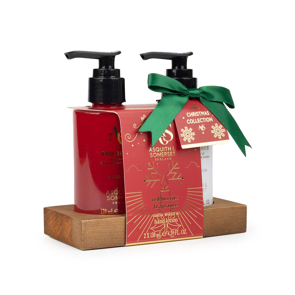 A gift set of two Asquith & Somerset hand and body care products displayed on a wooden base. The set includes a red hand soap bottle and a white lotion bottle, both with black pumps, wrapped in a red holiday-themed paper sleeve with a green ribbon bow and a 'Christmas Collection' tag.