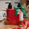 Two Asquimol Soap Company hand wash bottles in a Christmas-themed presentation. One bottle is red with gold lettering and the other is white with gold lettering, both with black pumps.