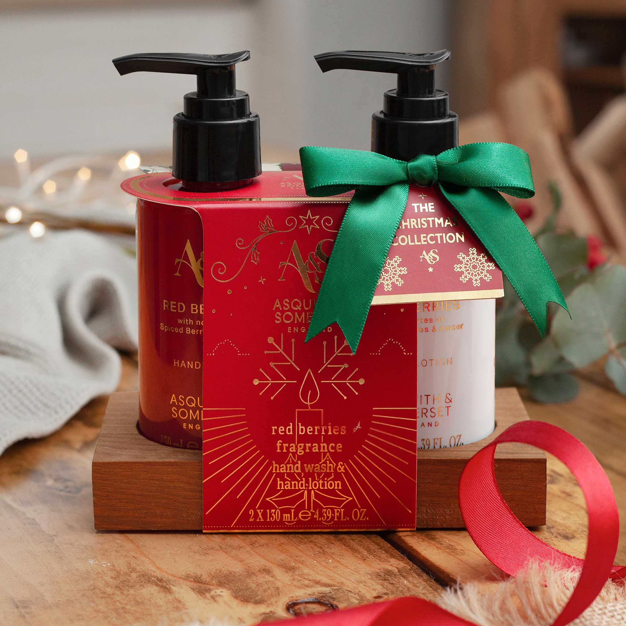 Two Asquimol Soap Company hand wash bottles in a Christmas-themed presentation. One bottle is red with gold lettering and the other is white with gold lettering, both with black pumps.