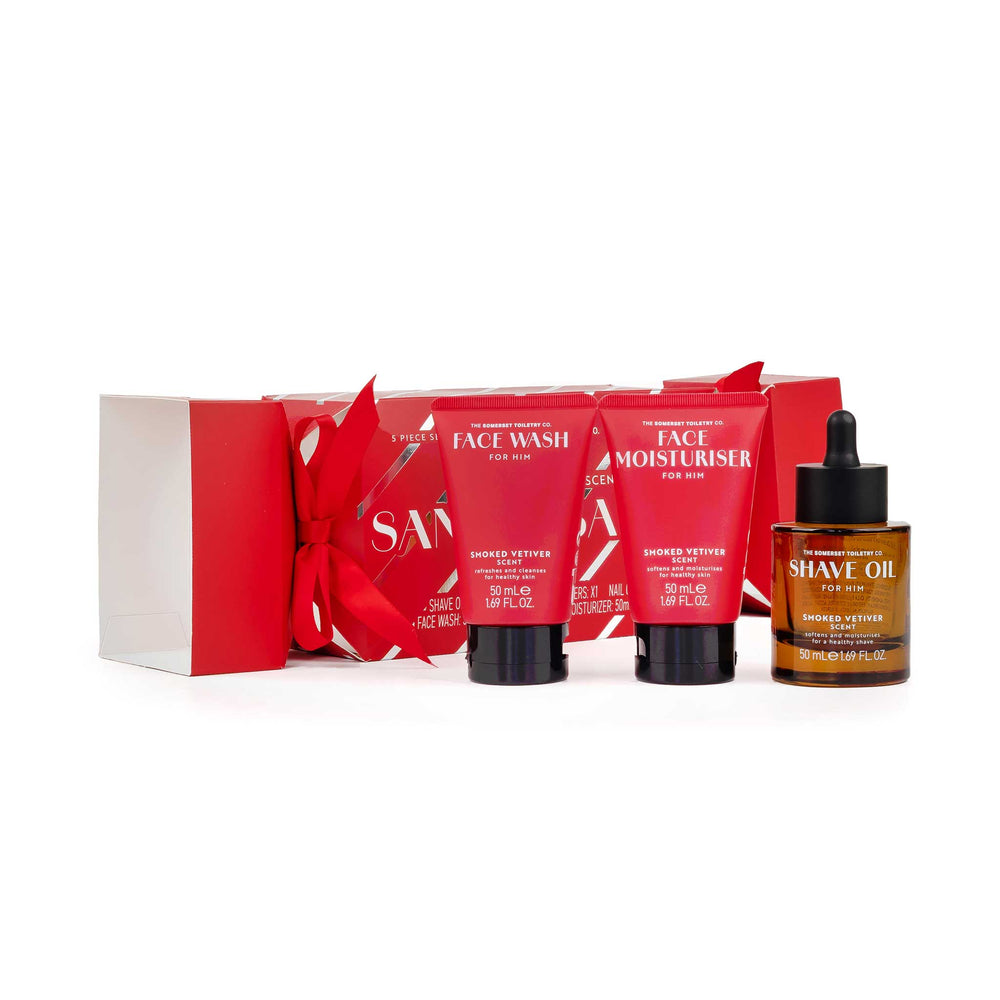 A men's grooming gift set featuring two red tubes of shower butter, a brown glass bottle of shave oil, and a red gift box with a ribbon bow, all on a white background.