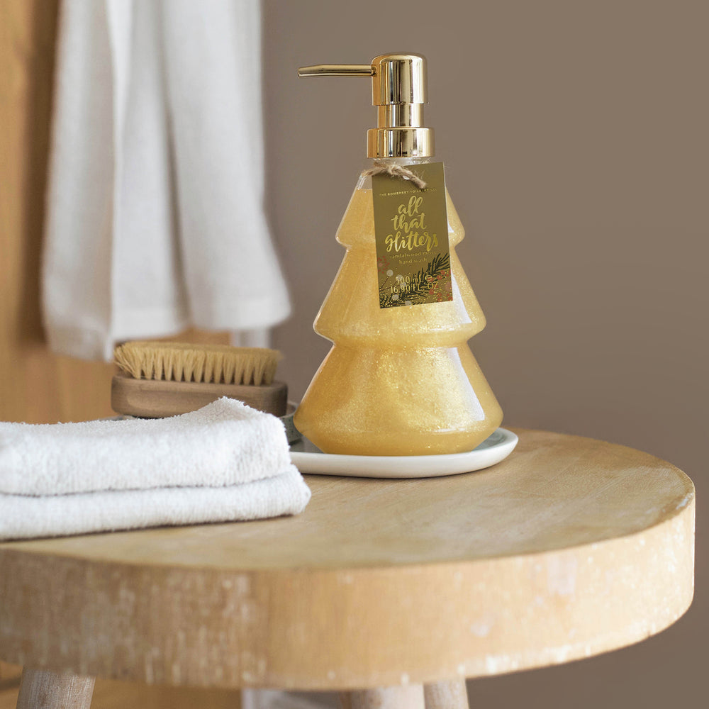 Tree-shaped soap dispenser on a wooden table with towels and a brush in the background