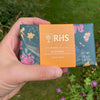 A person holding a large bar of RHS wild moss soap with a lawn and flower borders out of focus behind.
