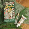Winter Woodland Festive Set gift collection with perfume rollerball, hand cream, and packaging on a green fabric background.