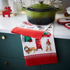 Green casserole dish on a kitchen counter with a festive towel featuring Christmas-themed designs.